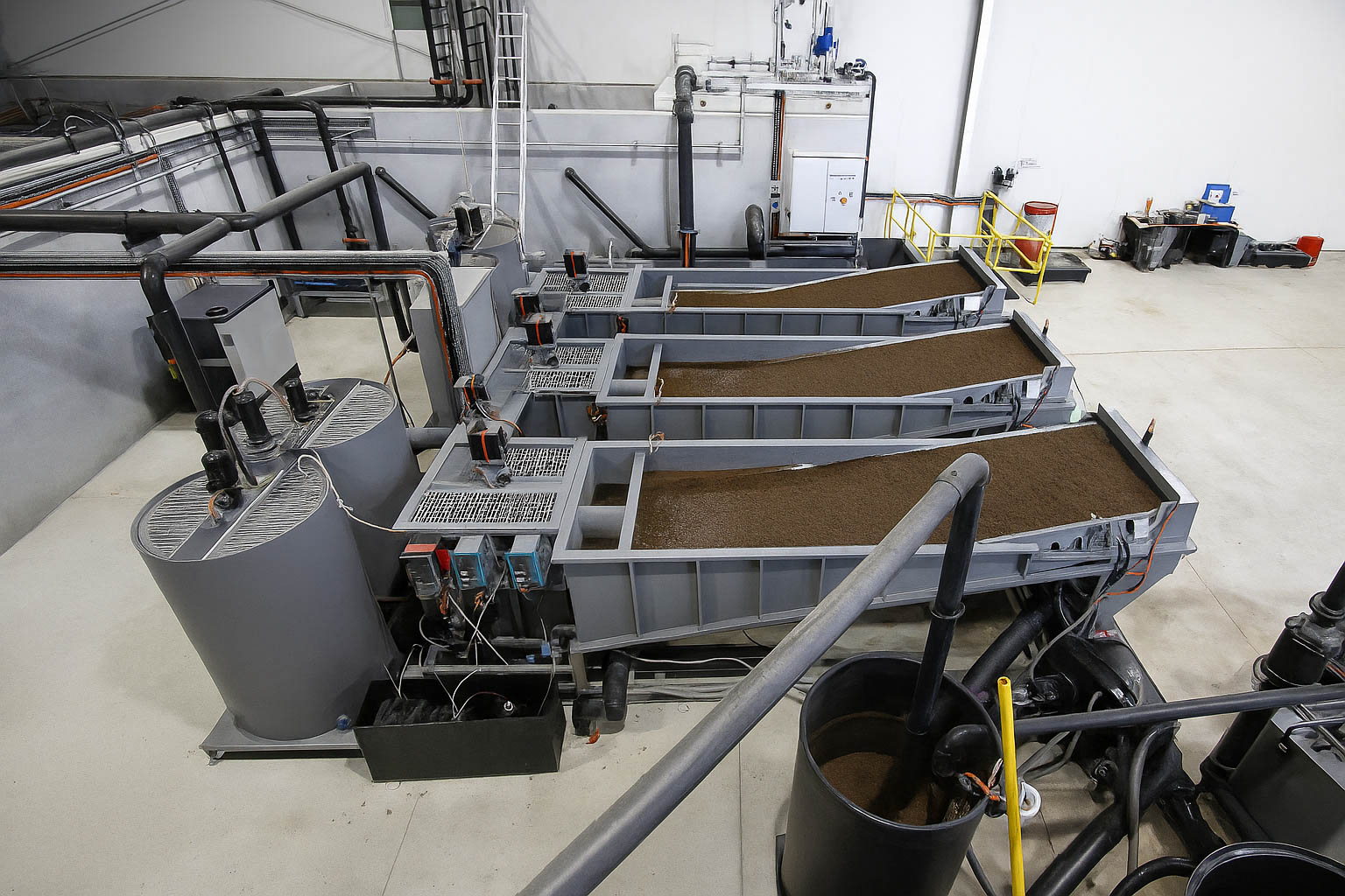 Técnico inspeccionando una planta de tratamiento de aguas residuales modular de color verde marca BIOMAX SYNERTECH, que incluye módulos de pretratamiento, decantación, DAF y oxidación avanzada. La planta está ubicada en un entorno industrial con techo alto y tuberías visibles. - ver más información